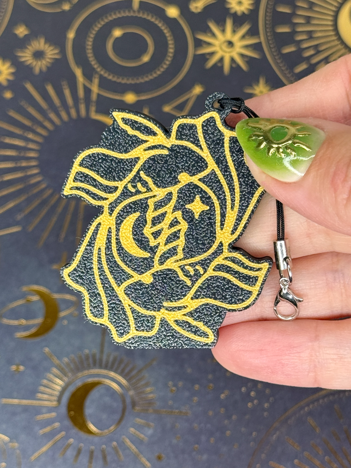 Hand holding a Tab Buddy keychain with a gold and black Pisces Zodiac design against a patterned background