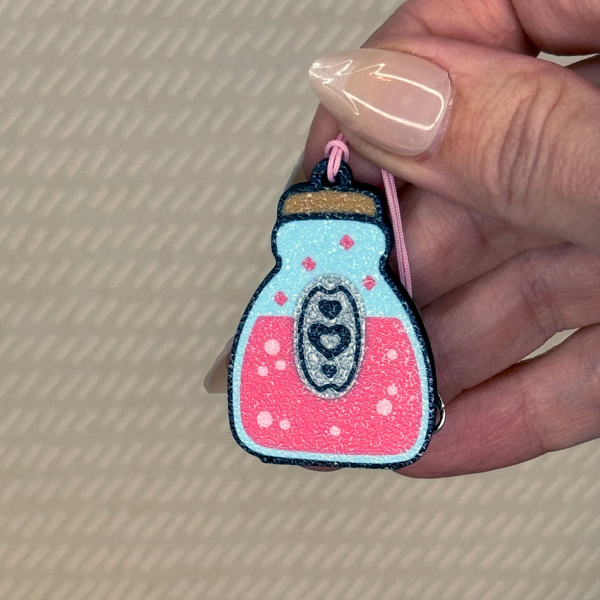 Hand holding a pink potion Tab Buddy keychain with a heart design on a beige background