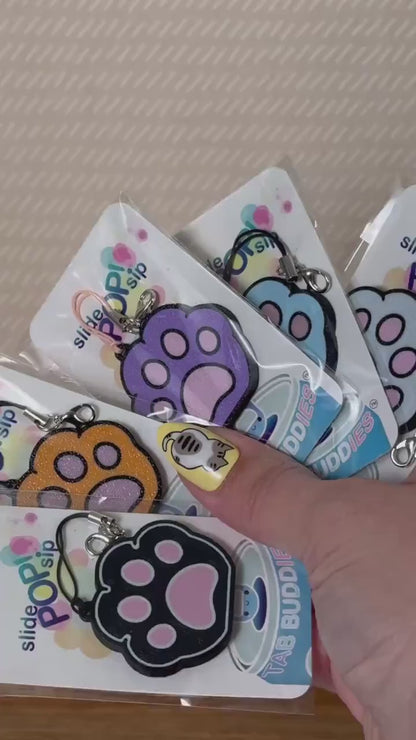 A grey and pink kitty paw Tab Buddy is used to open a red can of Coca-Cola. Other various colored paw Tab Buddies in their packaging also are displayed.