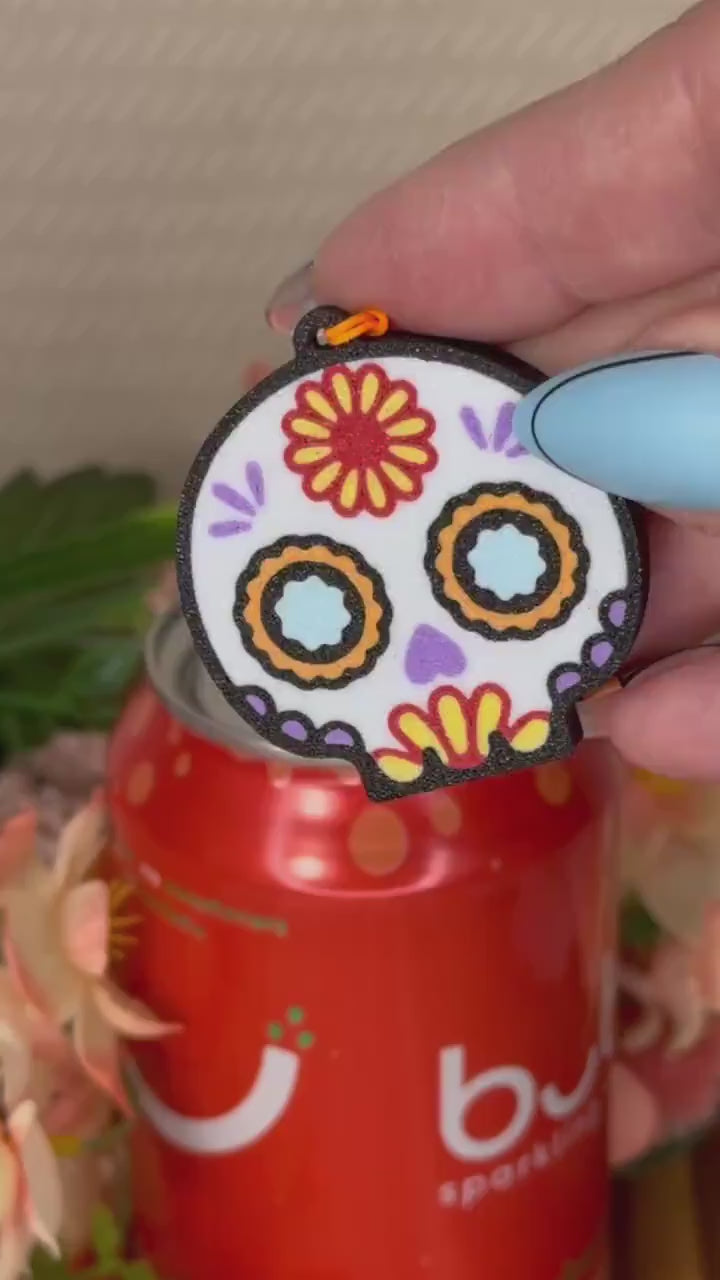 A Sugar Skull Tab Buddy opens a red can of Bubly. Subsequent images show other related skull designs of Tab Buddies.