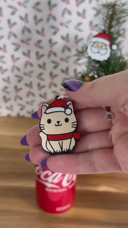 A beige cartoon style cat wearing a red scarf and Santa hat opens a red can of Coca-Cola. Subsequent images show other related Christmas-themed designs of Tab Buddies including a Santa face and a Christmas tree.