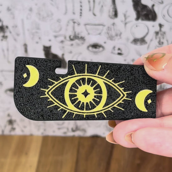 Two black and gold Tab Buddy XL designs are shown as complements to the Zodiac series of soda Tab Buddies. One then is shown opening a can of soup by lifting the tab and peeling back the lid while surrounded by the Zodiac Tab Buddies.