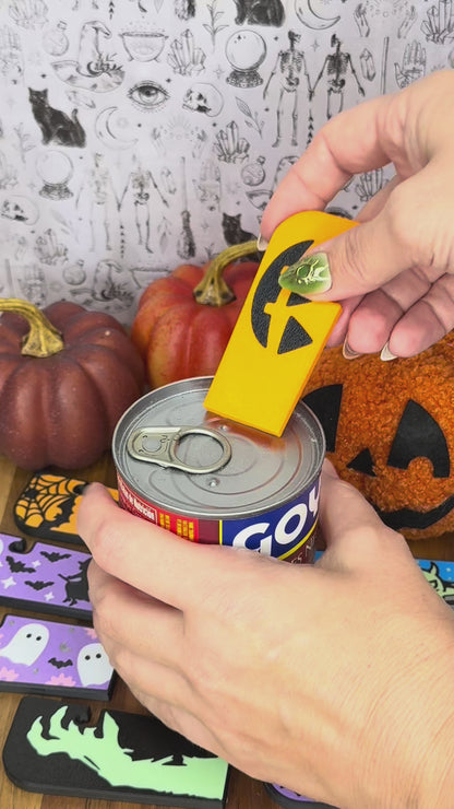 A Jackolantern design Tab Buddy XL opens a can of bean soup by lifting the tab and peeling back its lid. Other Halloween themed designs of Tab Buddy XLs then are displayed.