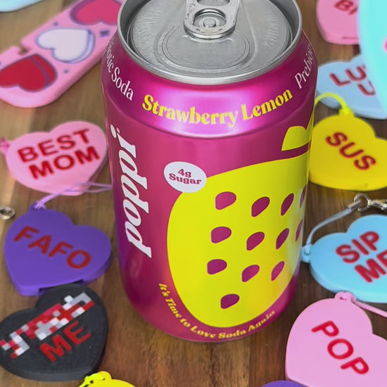 A "Tru Luv" Candy Heart Tab Buddy is used to open a can of Poppi soda. Colorful Candy Hearts Tab Buddies with different messages are displayed around the can.