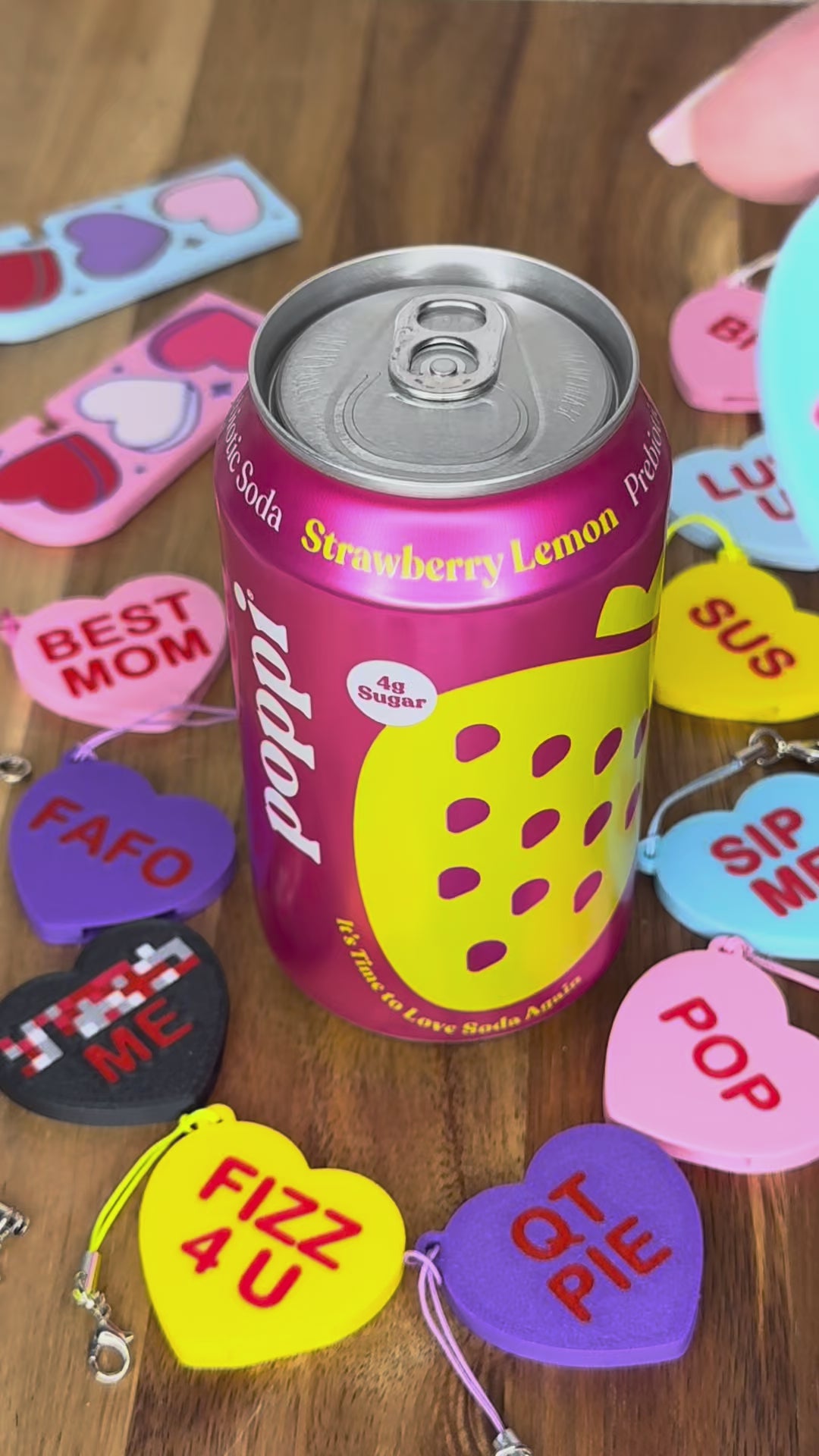 A "Tru Luv" Candy Heart Tab Buddy is used to open a can of Poppi soda. Colorful Candy Hearts Tab Buddies with different messages are displayed around the can.