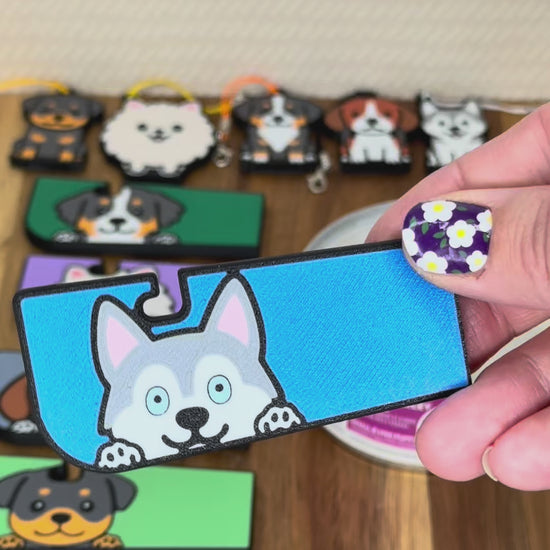 A Tab Buddy XL is shown lifting the tab of a can of dog food, then peeling back the lid. A smaller Tab Buddy is shown opening an energy drink can. Various dog designs of both sizes are shown.