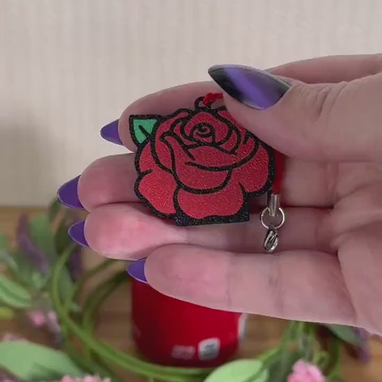 A red rose Tab Buddy opens a red can of Coca-Cola resting on a wooden surface surrounded by a wreath of pink and purple flowers.