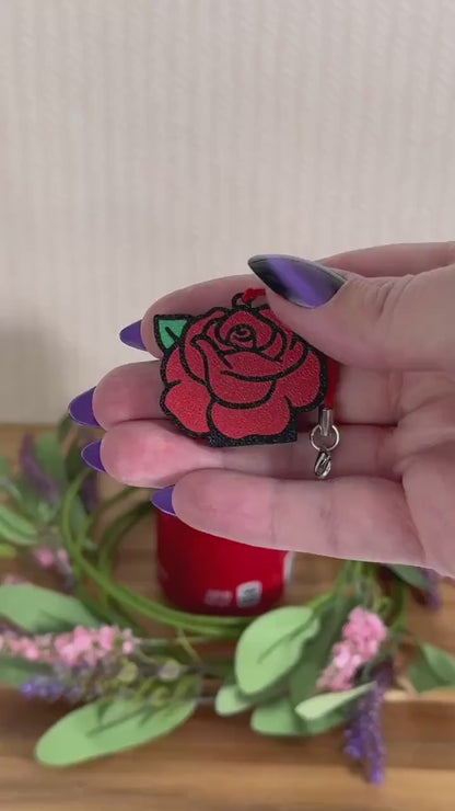 A red rose Tab Buddy opens a red can of Coca-Cola resting on a wooden surface surrounded by a wreath of pink and purple flowers.