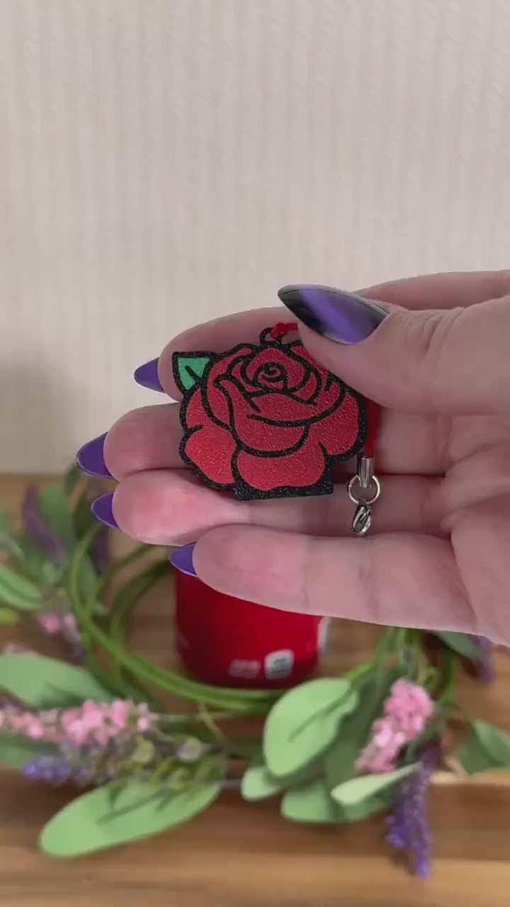 A red rose Tab Buddy opens a red can of Coca-Cola resting on a wooden surface surrounded by a wreath of pink and purple flowers.