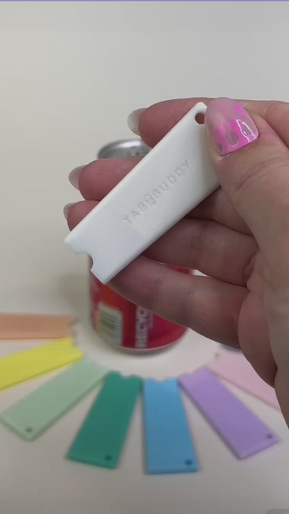 A white Tab Buddy Classic is used to open a red can of Coca-Cola. Other colorful Tab Buddy Classics surround the can.