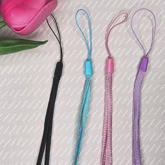 A black wrist strap is attached to a white kitty Tab Buddy XL, then a pink wrist strap is attached to a pink strawberry soda Tab Buddy.  The XL then is used to open a can of pineapple, with text on the videe explaining that the strap slides out of the way while peeling back lids.