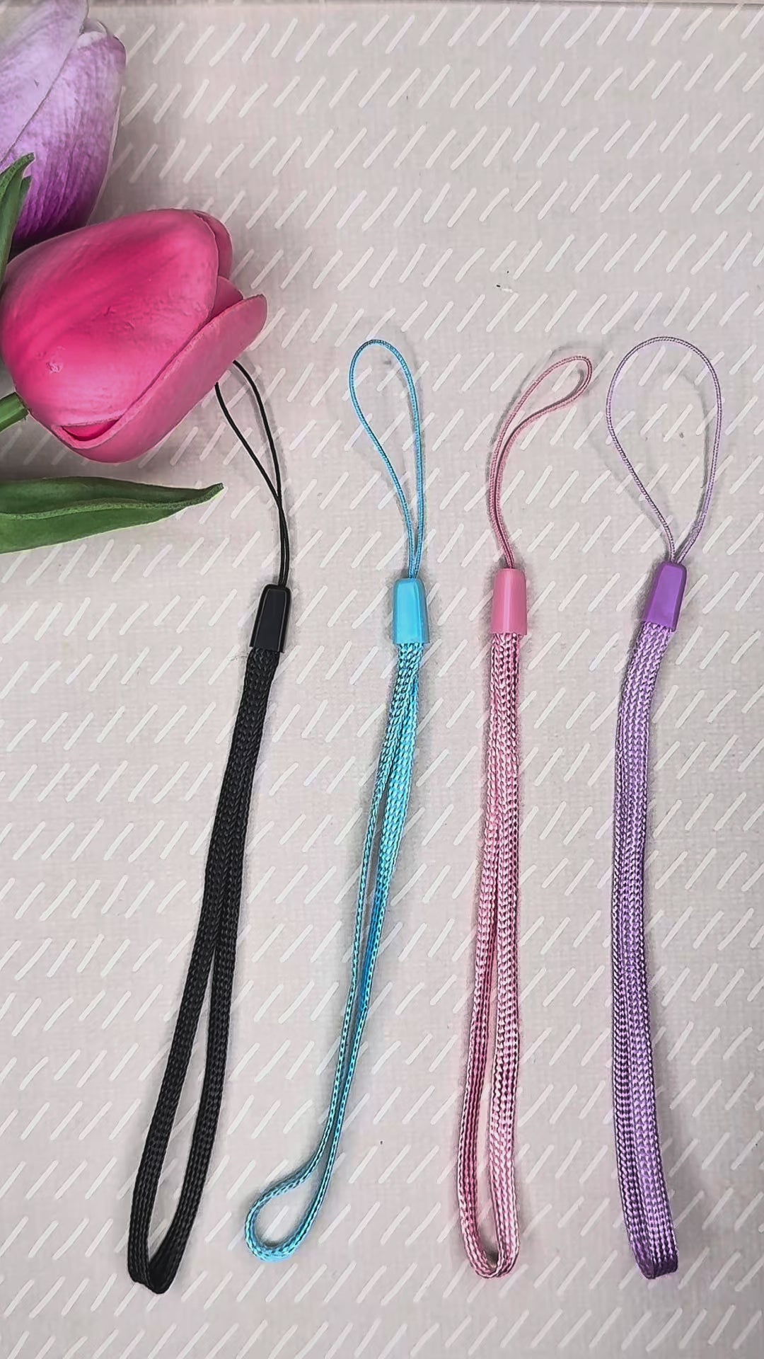 A black wrist strap is attached to a white kitty Tab Buddy XL, then a pink wrist strap is attached to a pink strawberry soda Tab Buddy.  The XL then is used to open a can of pineapple, with text on the videe explaining that the strap slides out of the way while peeling back lids.