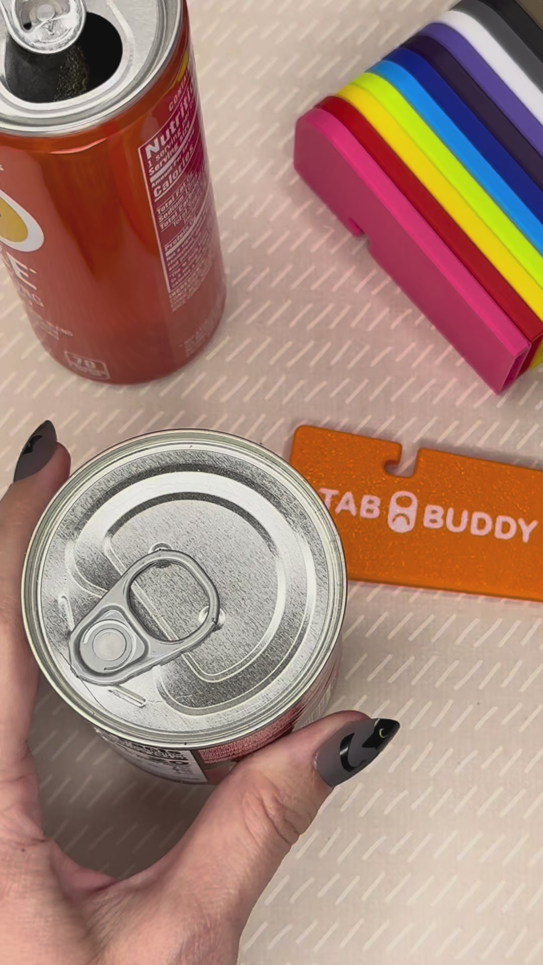 A turquoise Tab Buddy XL is used to lift the tab, then peel back the lid on a can of chipotle peppers. An Orange Tab Buddy XL then is used to pop the tab of an orange can of soda. A range of Tab Buddy XL colors then are shown.