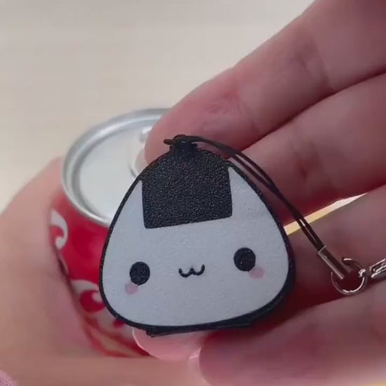 An onigiri rice ball-shaped Tab Buddy is used to open a red can of Coca-Cola.