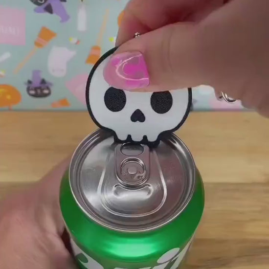 A white skull Tab Buddy is used to open a green can of Sprite. A Candy corn themed Tab Buddy then opens a red can of Coca-Cola. Subsequent images show other related Halloween-themed Tab Buddies designs.