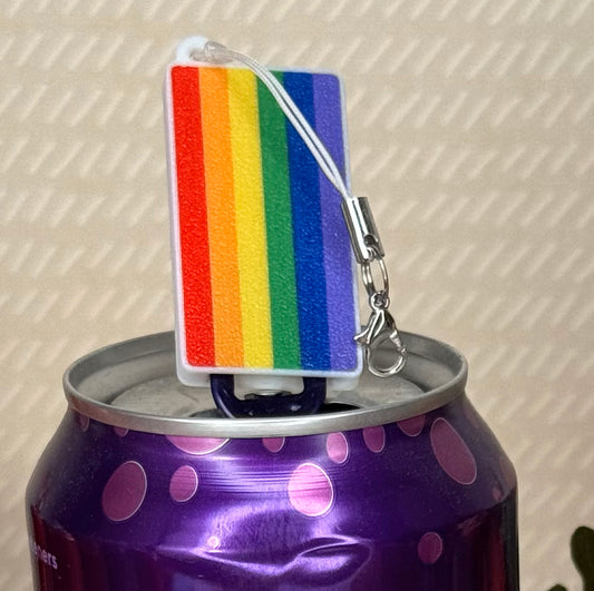 Rainbow striped Tab Buddy keychain rests atop a purple can with pink polka dots.