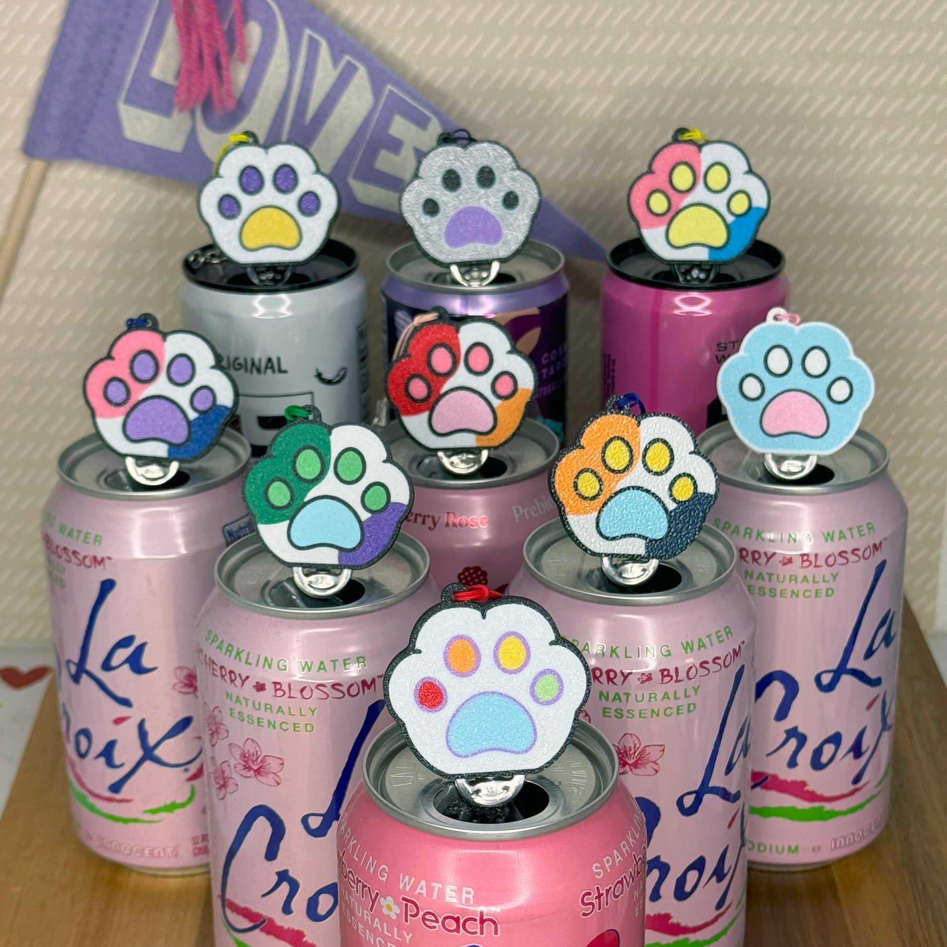 Set of sparkling water cans with colorful paw-shaped Tab Buddies Pride Paws on a wooden surface.