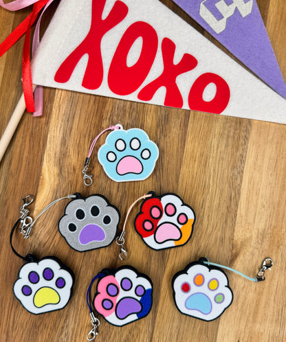 Colorful paw print Tab Buddies in Pride Flag color combinations on a wooden surface with 'XOXO' banner in the background