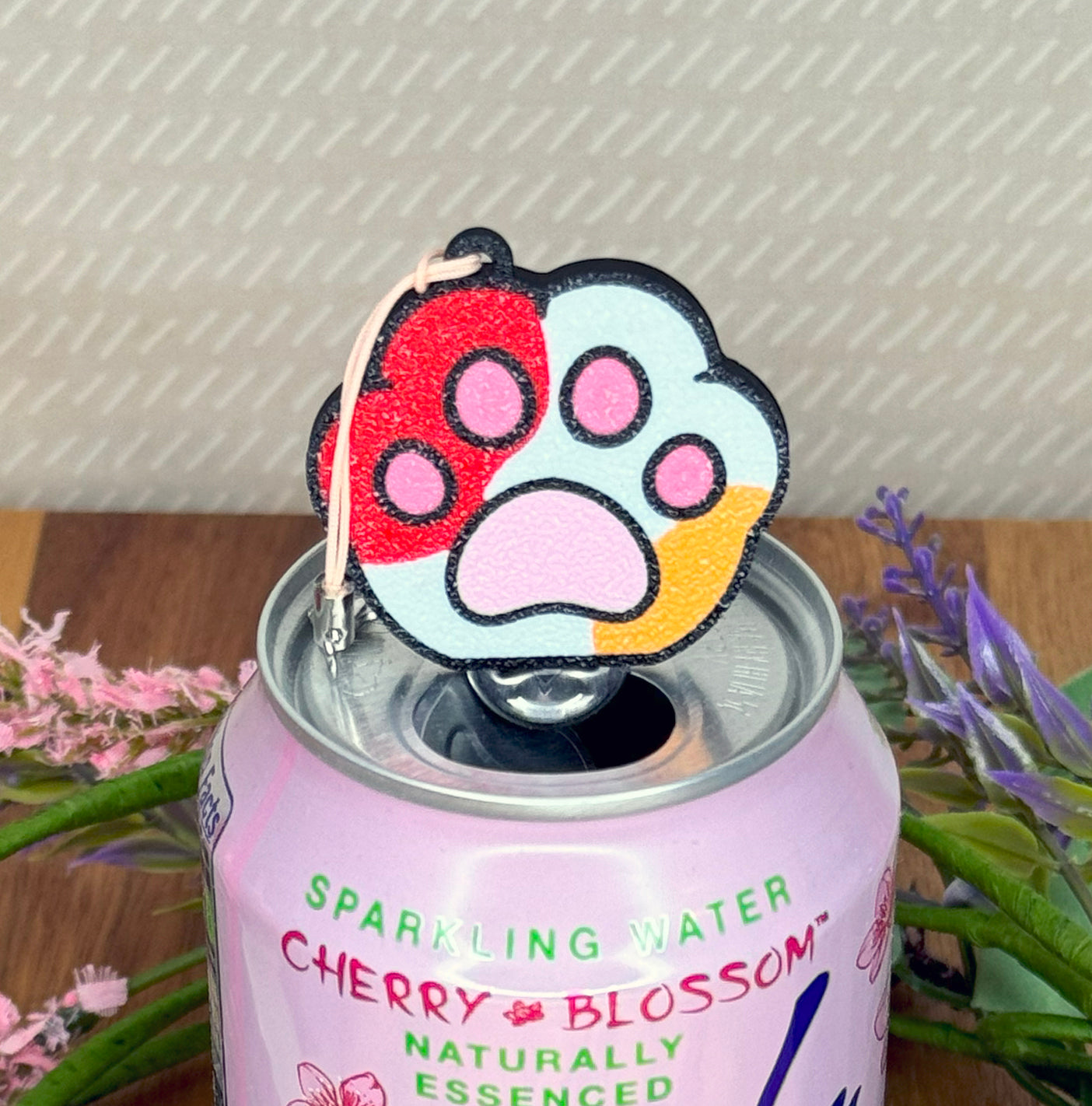 Pink cherry blossom sparkling water can with a colorful paw-shaped Tab Buddy on top, surrounded by flowers.