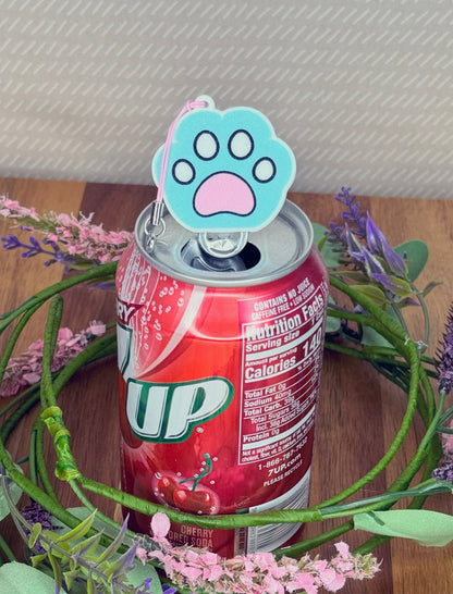 Can of 7-Up with a blue, white and pink paw print Tab Buddy keychain on a wooden surface with flowers