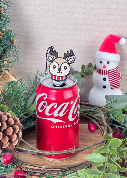 Coca-Cola can with a reindeer Tab Buddy resting on top and a decorative background with Christmas elements.