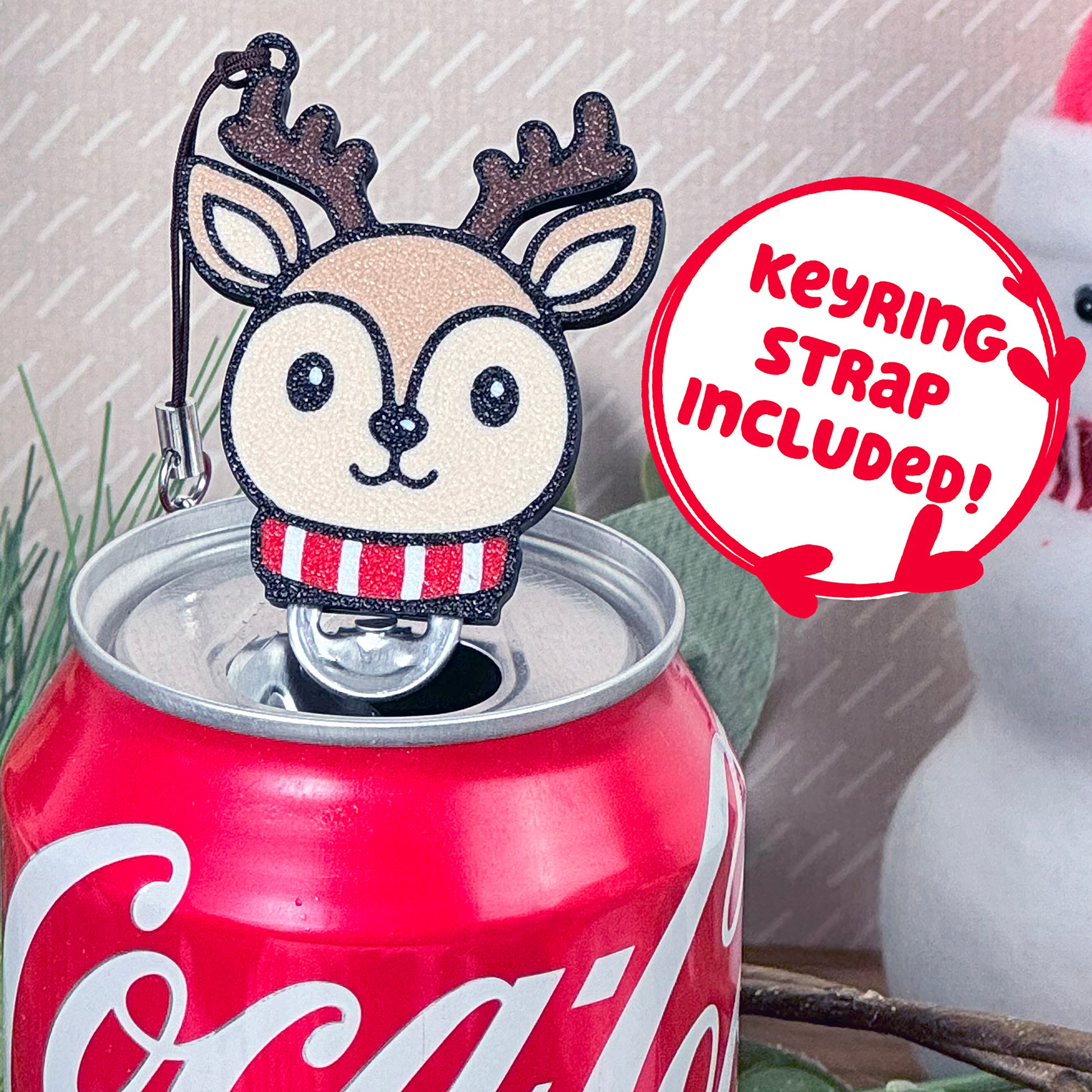 Coca-Cola can with a reindeer Tab Buddy resting on top, featuring a 'Keyring Strap Included!' text.