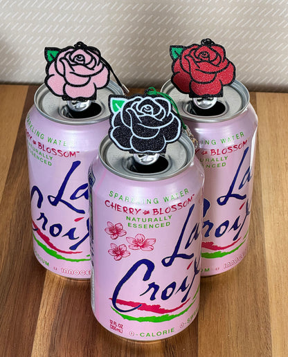 Three cans of La Croix sparkling water with decorative rose Tab Buddies on top on a wooden surface.