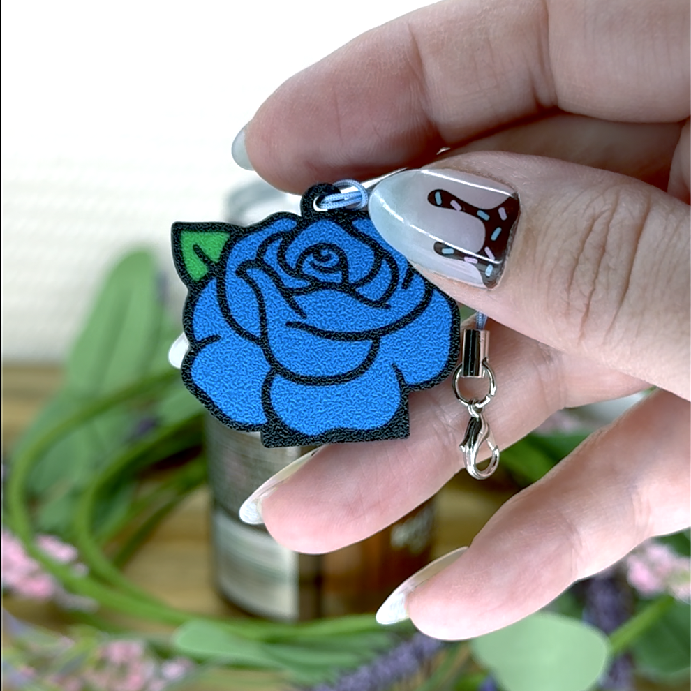 Hand holding a blue rose Tab Buddy keychain against a blurred natural background