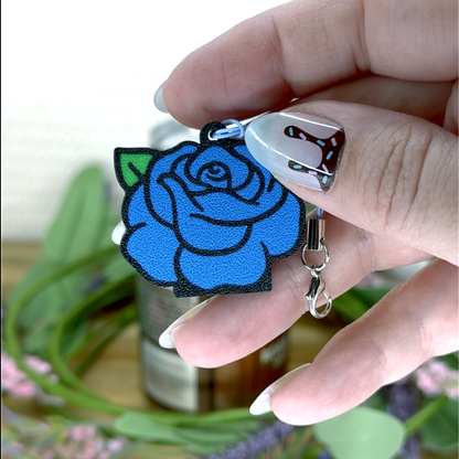 Hand holding a blue rose Tab Buddy keychain against a blurred natural background
