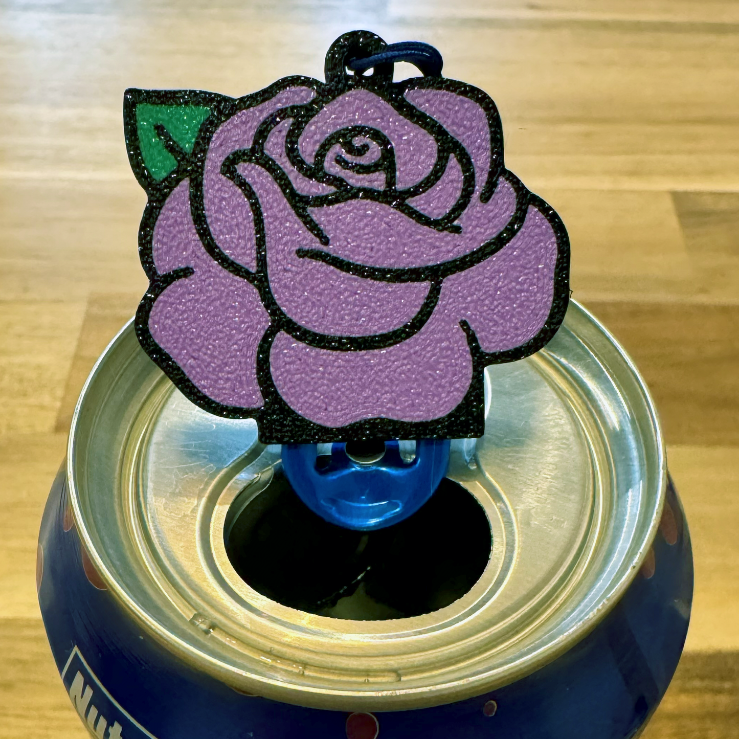 Purple rose-shaped Tab Buddy on a blue can with a wooden background