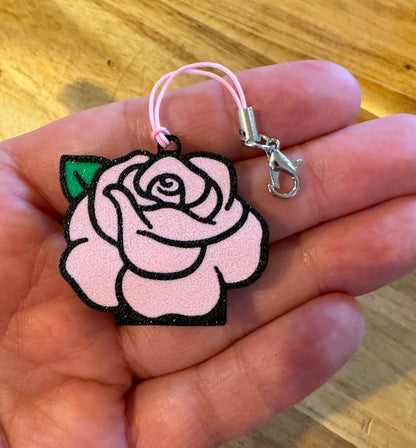 Pink rose-shaped Tab Buddy keychain held in a hand on a wooden surface