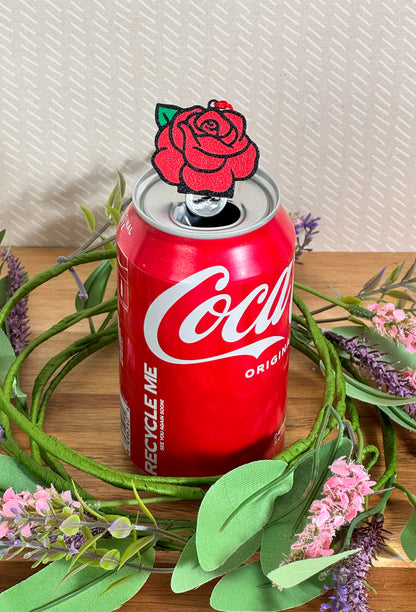 Red Coca-Cola can with a rose design Tab Buddy on top, surrounded by greenery and flowers.
