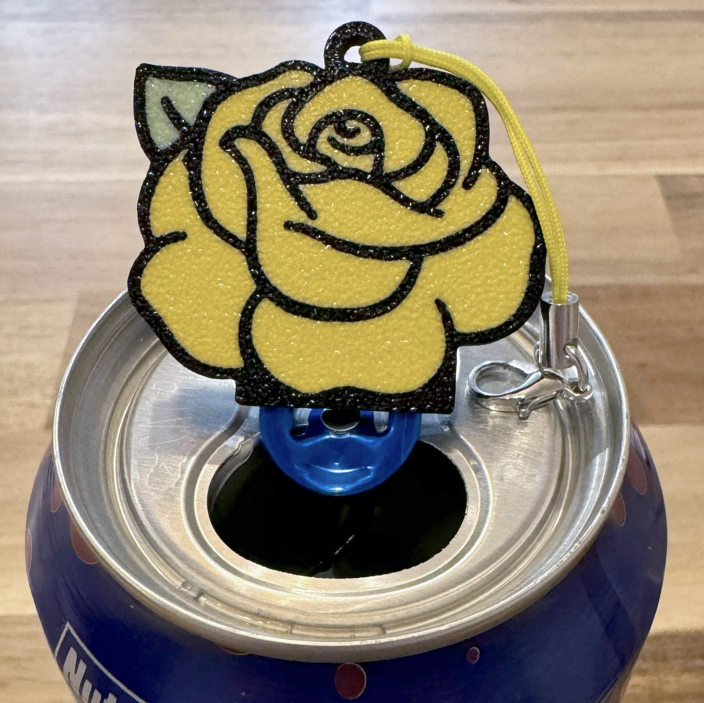 Yellow rose-shaped Tab Buddy on a blue can with a wooden surface background