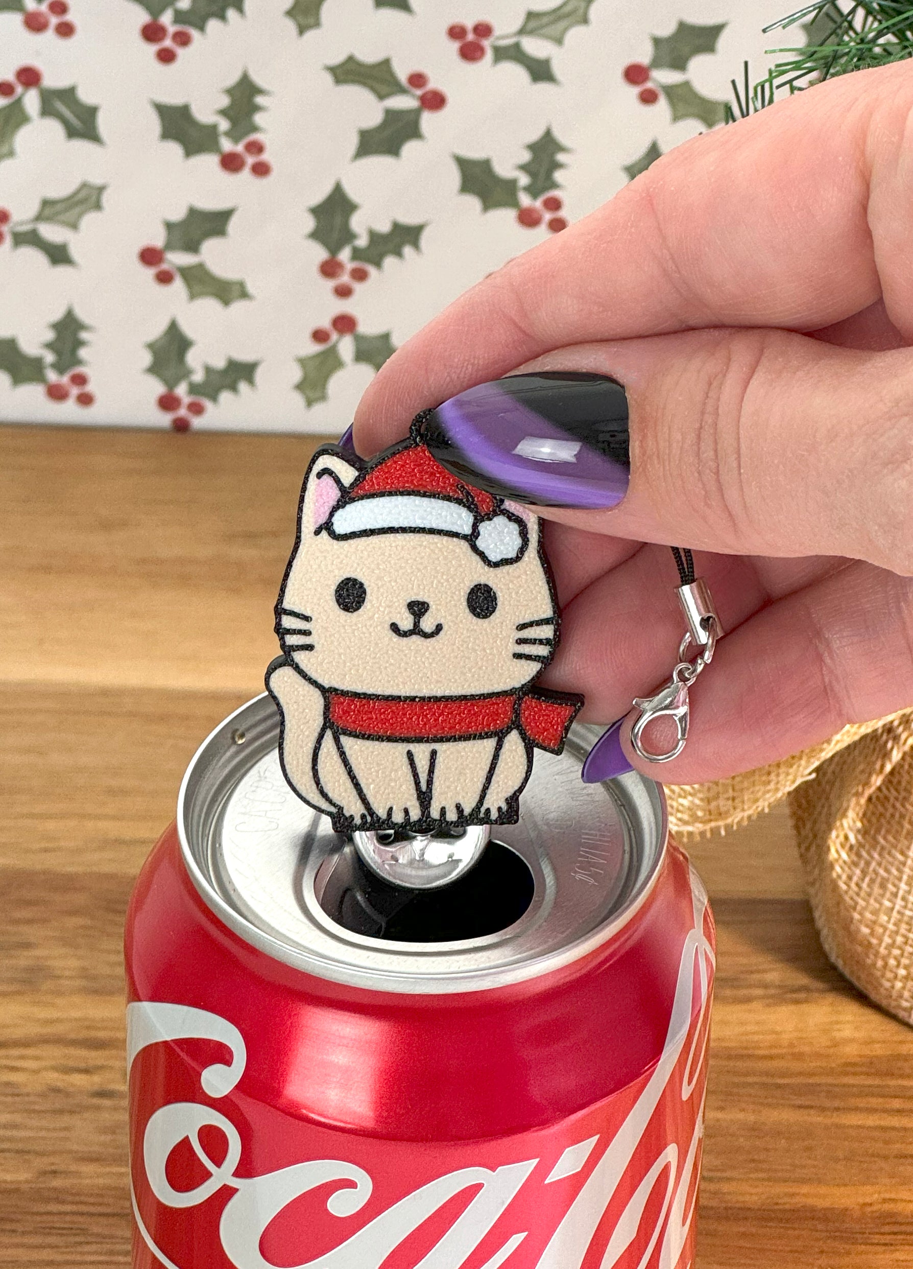 Coca-Cola can with a Santa cat-shaped Tab Buddy on a wooden surface