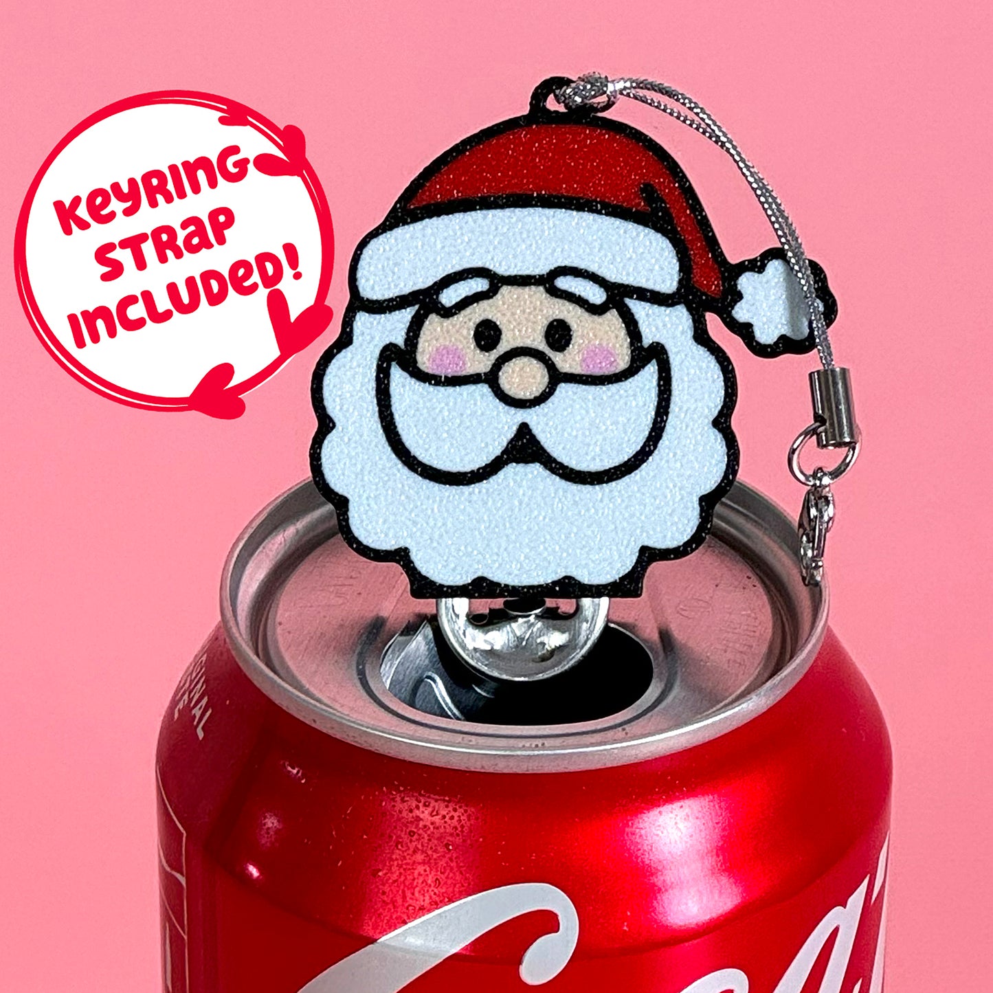 Coke can with a Santa Claus Tab Buddy keychain on a pink background. Text reads "keyring strap included."