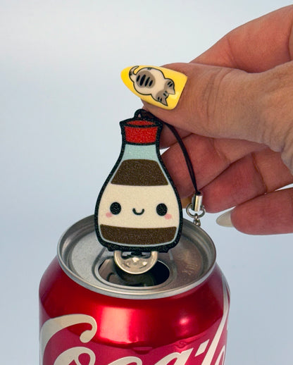 Hand holding a small bottle-shaped Tab Buddy keychain over a Coca-Cola can