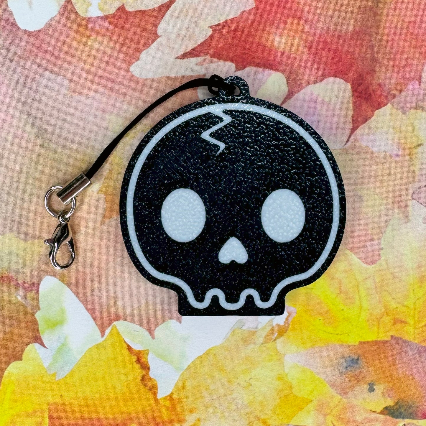 Black skull-shaped Tab Buddy on a colorful fall leaf background