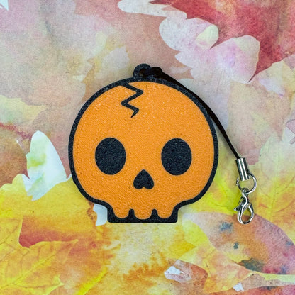 Orange skull-shaped Tab Buddy on a fall foilage background