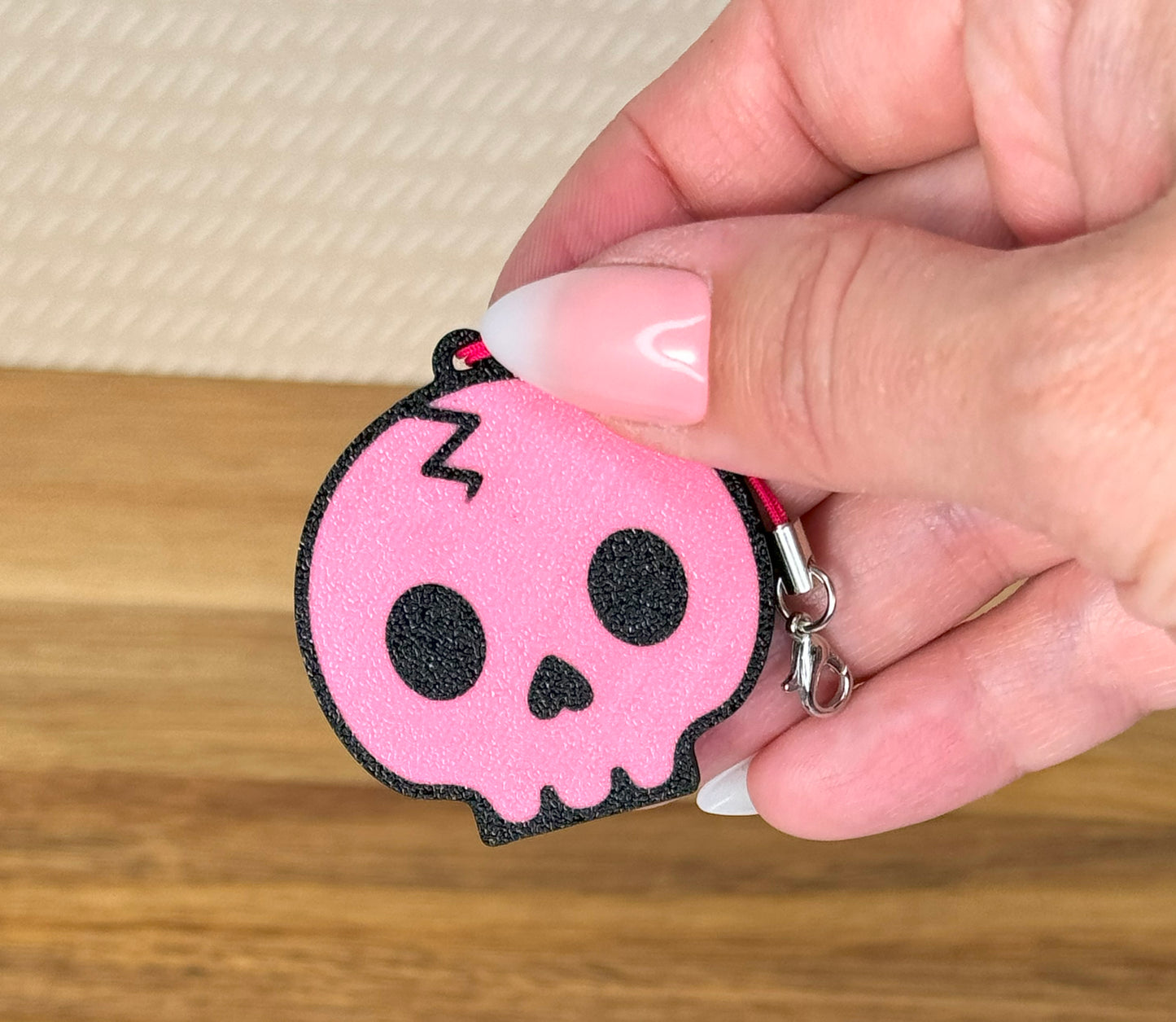 Pink skull-shaped Tab Buddy keychain held by a hand over a wooden surface