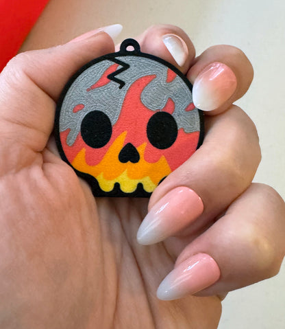 Hand holding a colorful skull-shaped Tab Buddy with fire designs against a neutral background