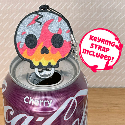 Flaming skull-shaped Tab Buddy with keyring strap rests atop a can of Cherry Coca-Cola