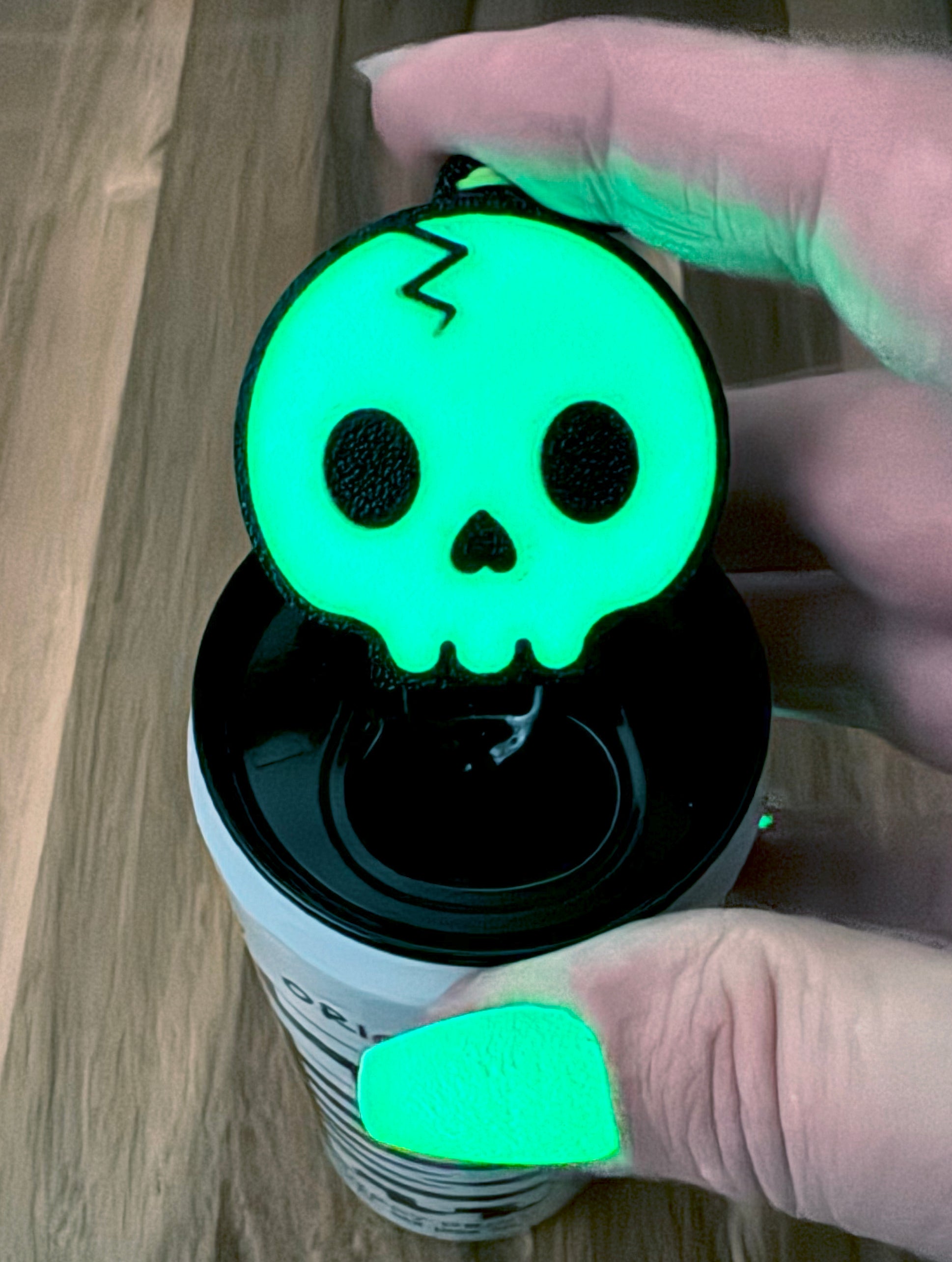 Person holding a glowing green skull-shaped Tab Buddy on top of a soda can with a wooden surface background