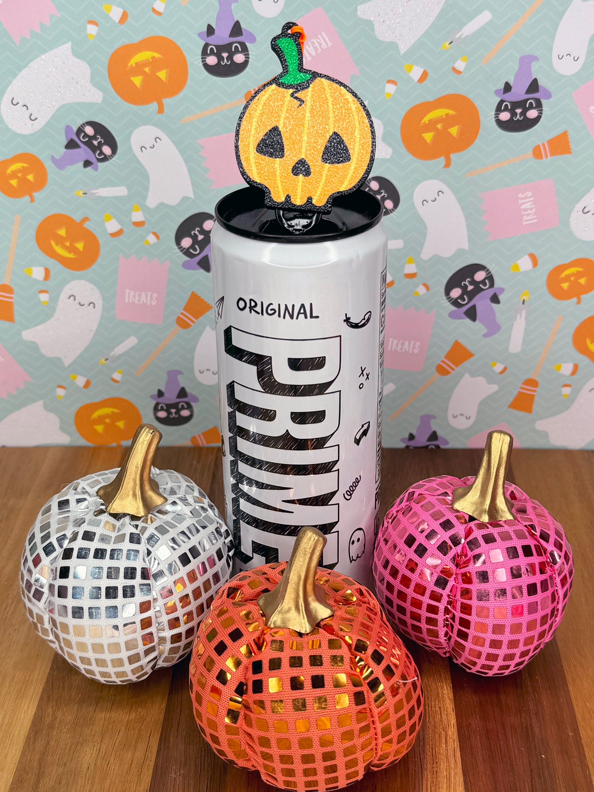 Energy drink can with a pumpkin skull-shaped Tab Buddy atop surrounded by pumpkins on a Halloween-themed background