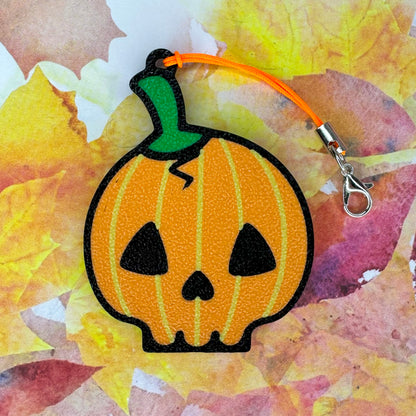 Pumpkin skull-shaped Tab Buddy  keychain with a green stem on a colorful leaf background