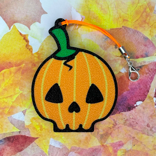 Pumpkin skull-shaped Tab Buddy  keychain with a green stem on a colorful leaf background