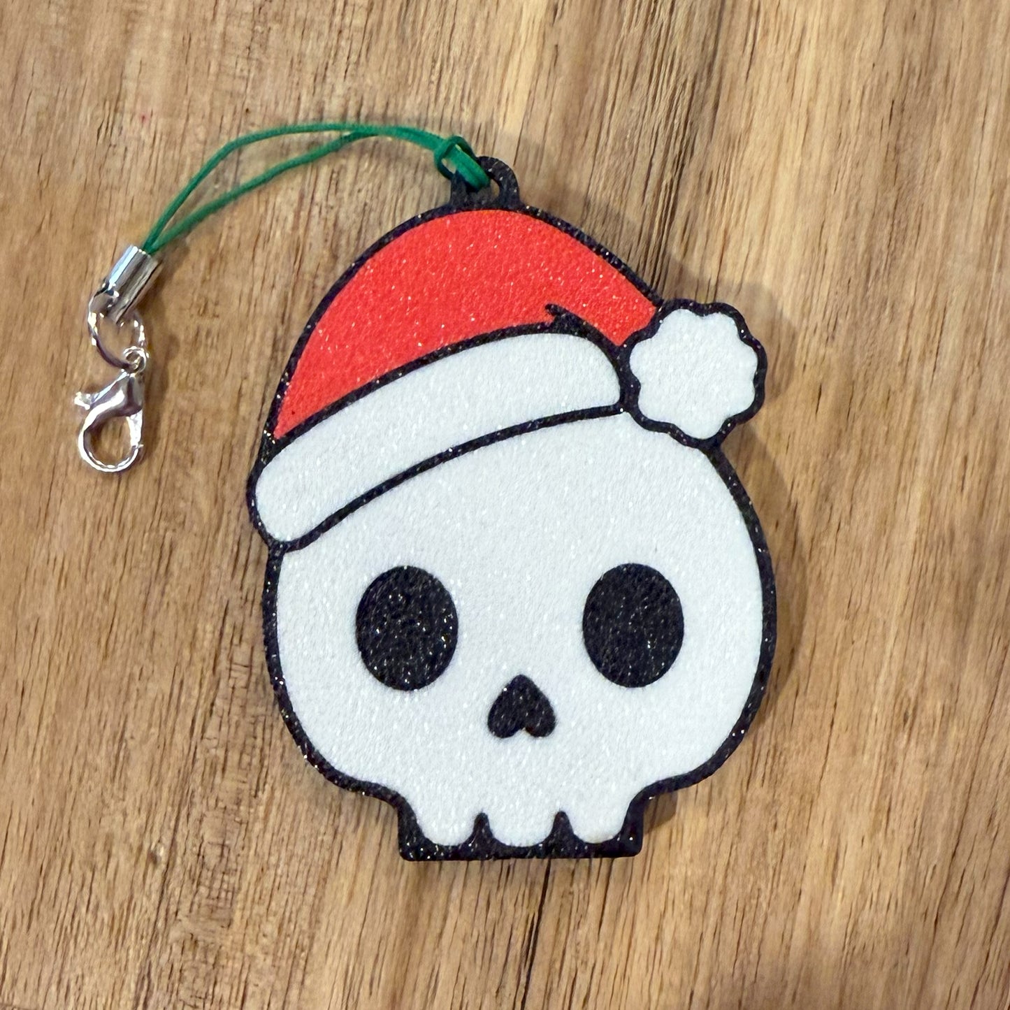 Skull-shaped Tab Buddy keychain with a red Santa hat on a wooden surface