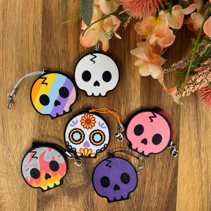 Colorful skull-shaped Tab Buddy keychains on a wooden background with flowers