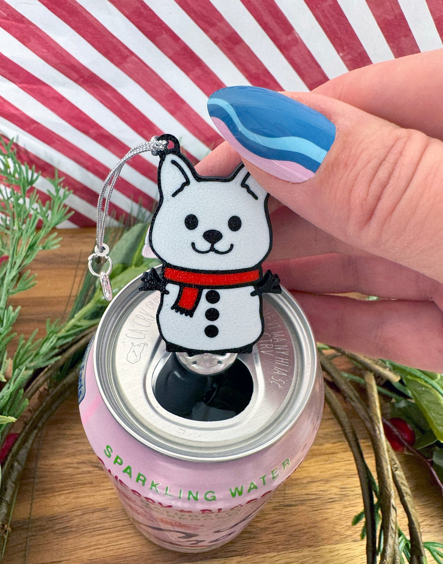 Tab Buddy keychain shaped like a snowman dog on a can of sparkling water with a striped background