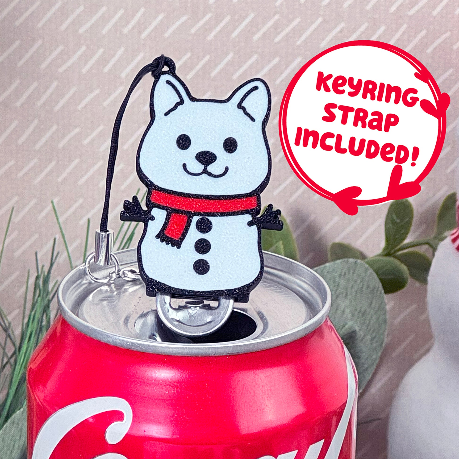 Coca-Cola can with a snowman dog Tab Buddy with keyring strap on a light background.