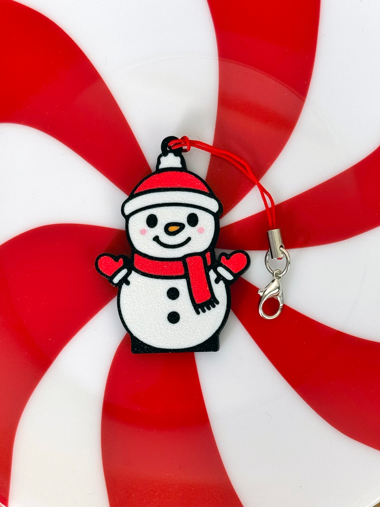 Snowman Tab Buddy keychain with red hat, gloves and scarf on a peppermint candy background